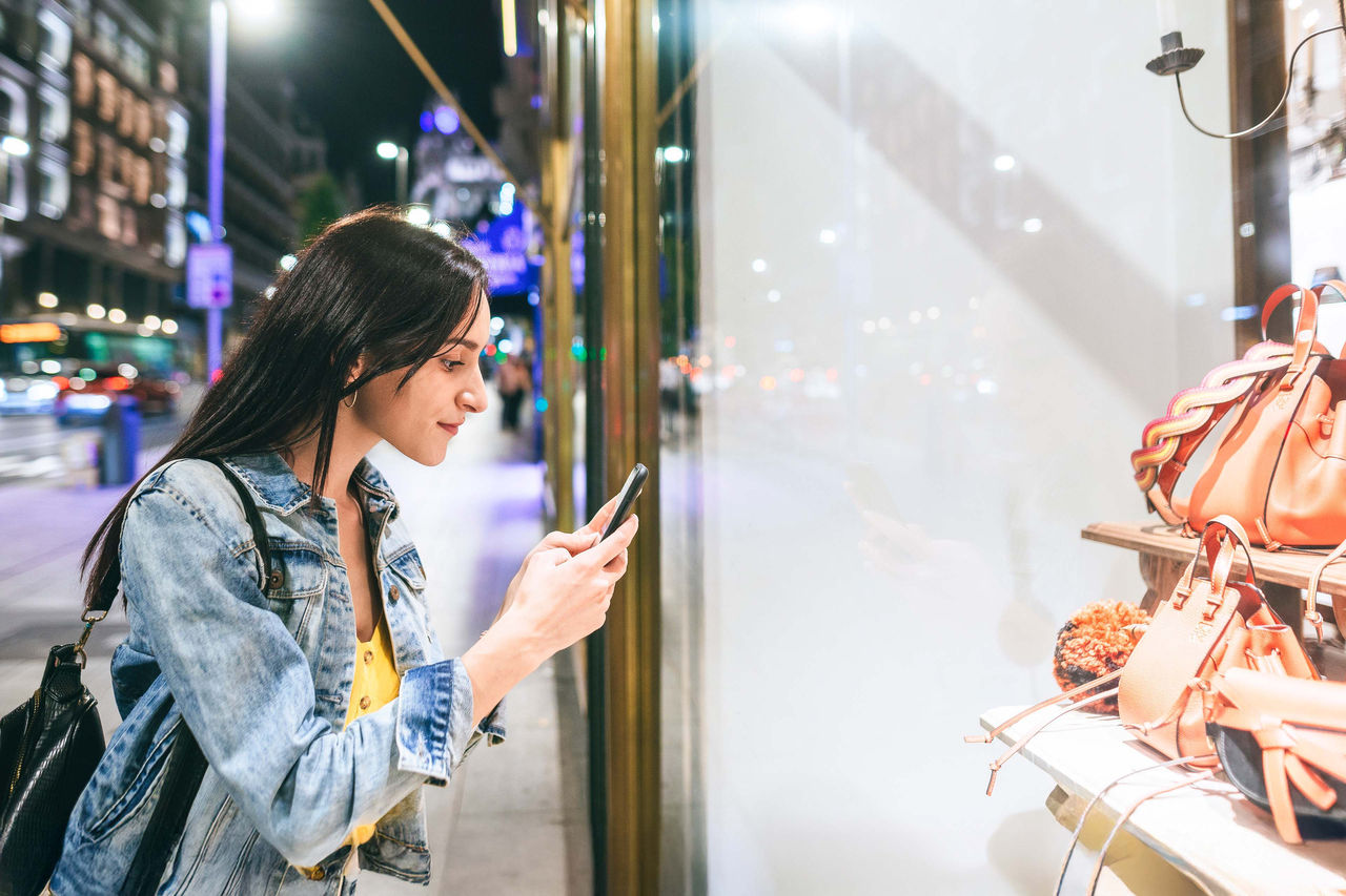 Woman taking a picture to shop window at night in Gran Via, Madrid
